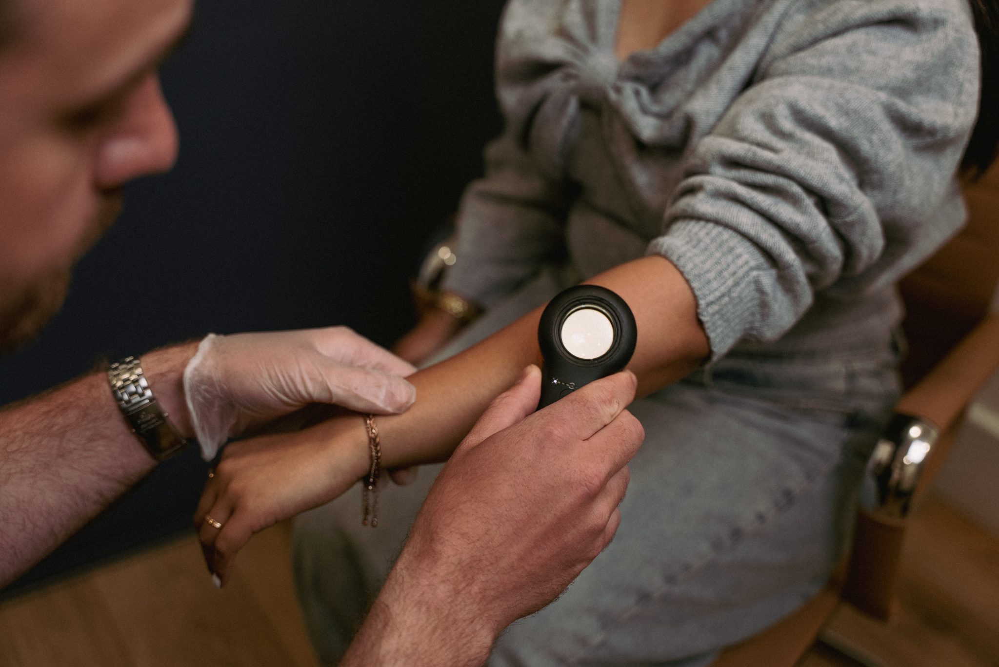 A clinician examining a patient's arm with a dermatoscope